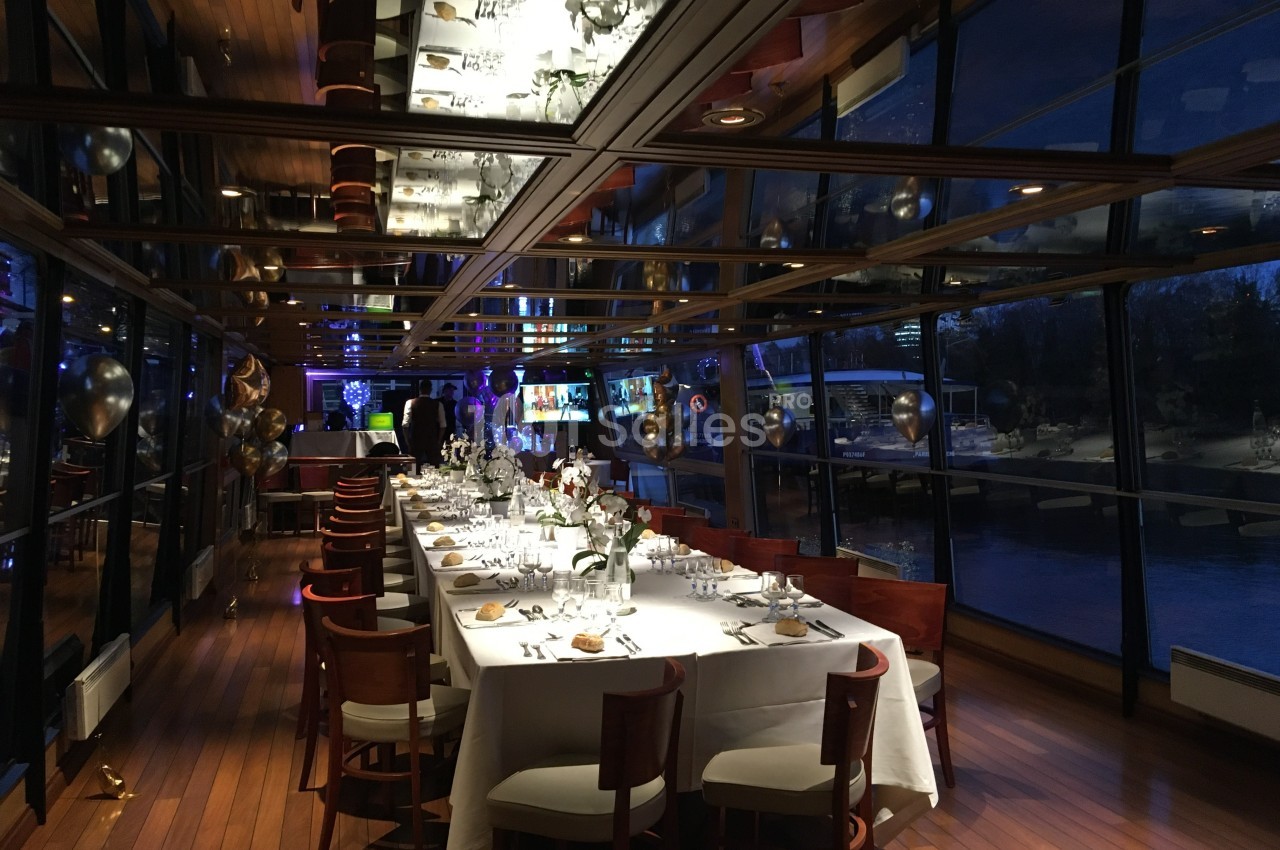 Salle de réception élégante avec grandes baies vitrées, tables dressées et éclairage tamisé en soirée.