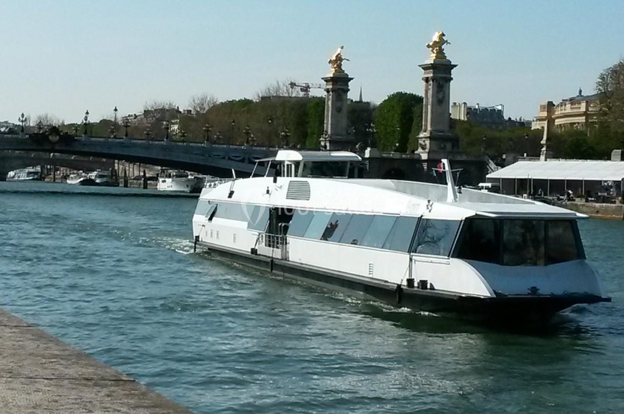 Bateau moderne naviguant sur une rivière avec un pont orné de statues dorées en arrière-plan.