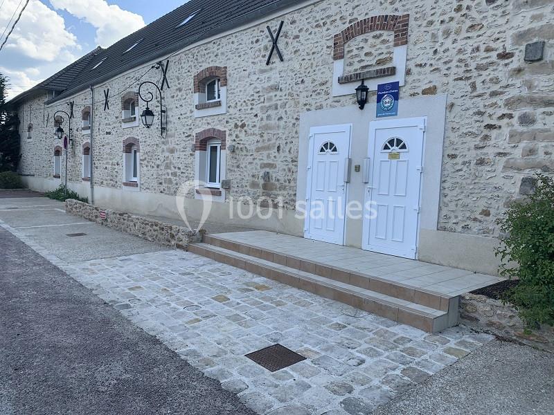 Façade en pierre d'un bâtiment avec deux portes blanches, lampadaires muraux et une rampe d'accès pavée.