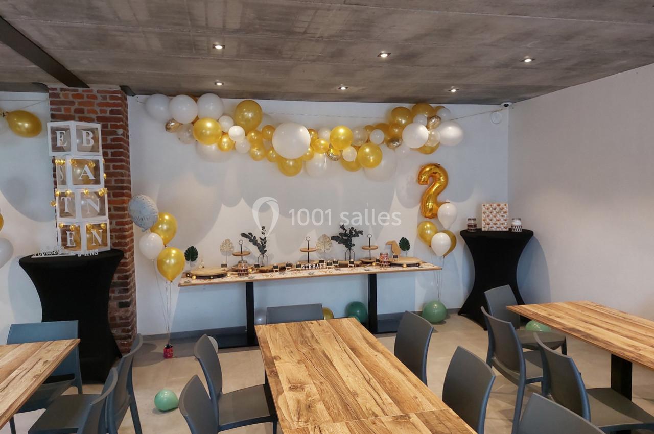 Salle décorée pour une fête avec des ballons blancs et dorés, une table de buffet et un chiffre 2 en ballon doré.