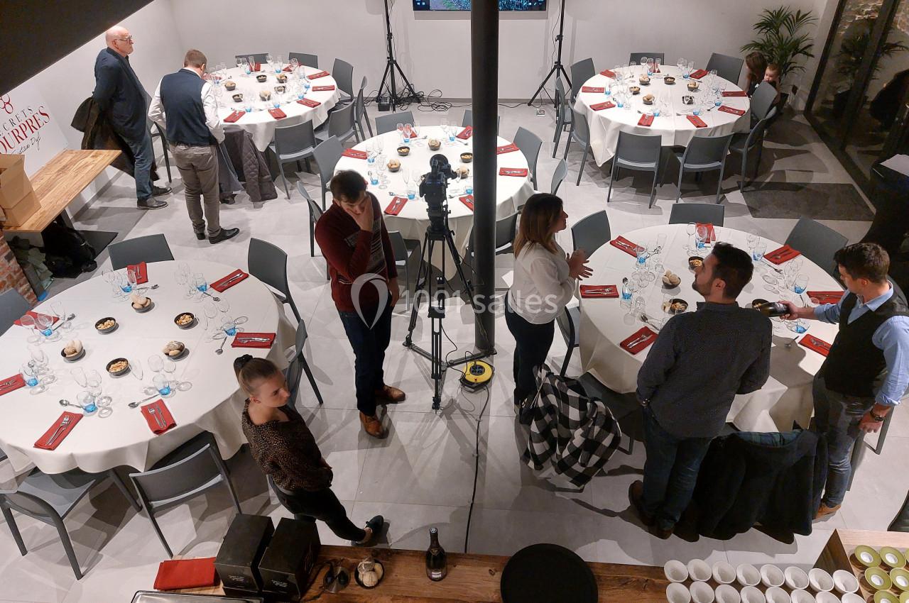 Salle aménagée avec des tables rondes dressées, des personnes discutent près d'un équipement de caméra.