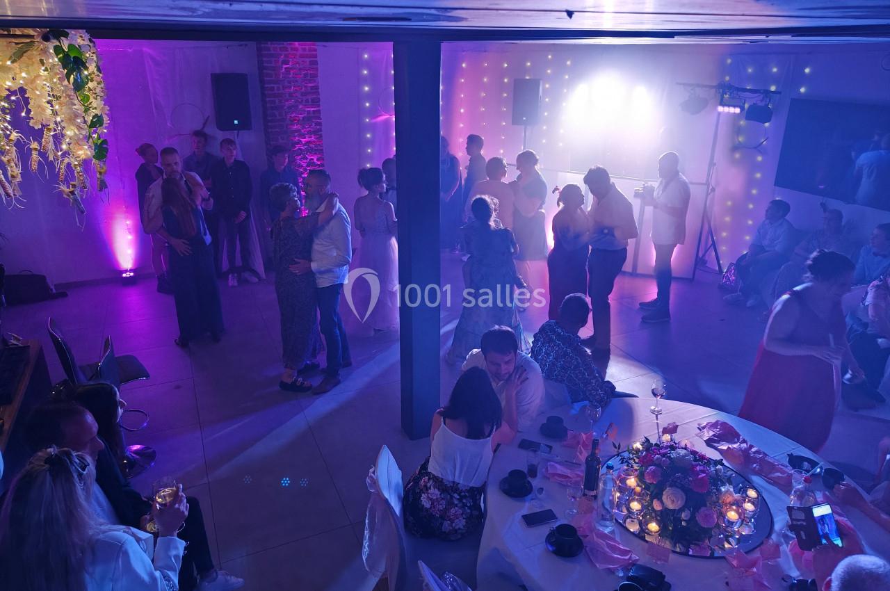 Des invités dansent et discutent dans une salle de réception décorée, éclairée par des lumières colorées.