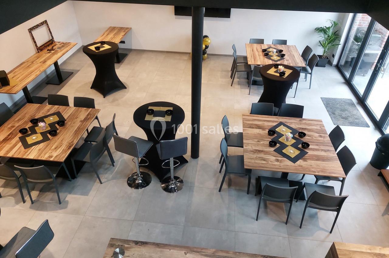 Salle moderne avec tables en bois, chaises grises et tables hautes, vue d'ensemble depuis un angle en hauteur.