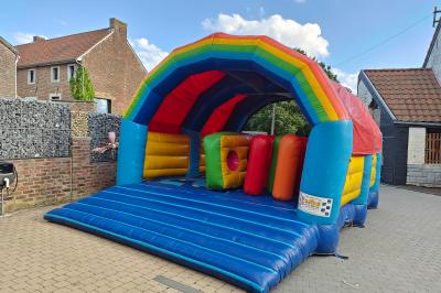 Structure gonflable colorée en forme d'arche, installée sur une cour pavée devant des maisons en briques.