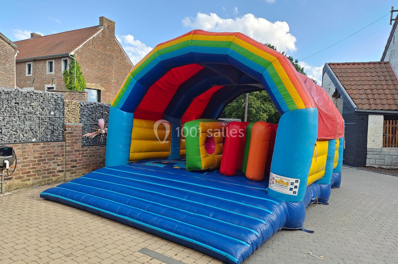 Structure gonflable colorée en forme d'arche, installée sur une cour pavée devant des maisons en briques.