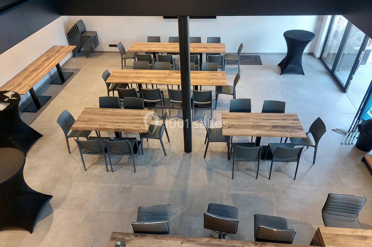 Salle moderne avec tables en bois, chaises grises et lumière naturelle entrant par de grandes baies vitrées.