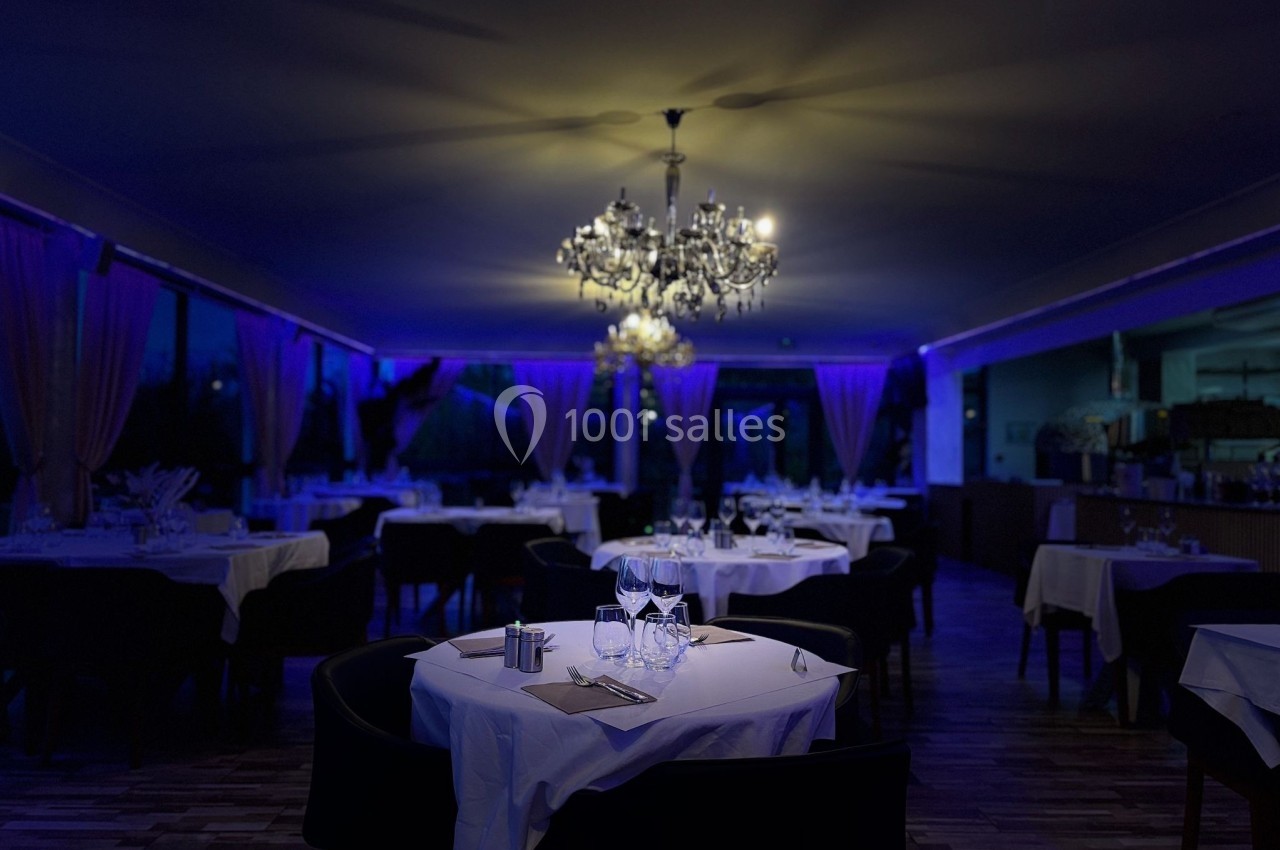 Salle de restaurant élégante éclairée par des lustres, avec tables dressées et ambiance tamisée.