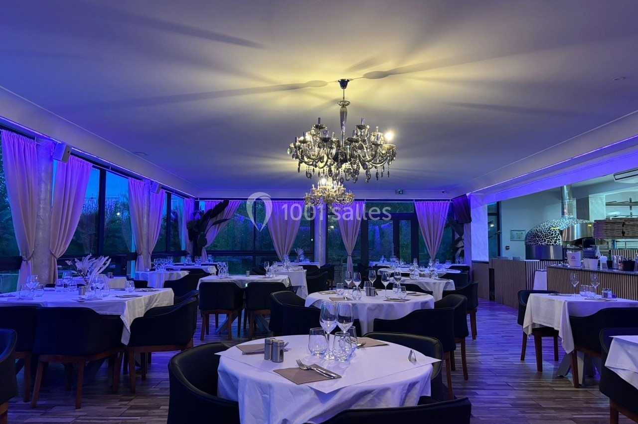 Salle de restaurant élégante avec tables dressées, nappes blanches, chandeliers et éclairage tamisé.