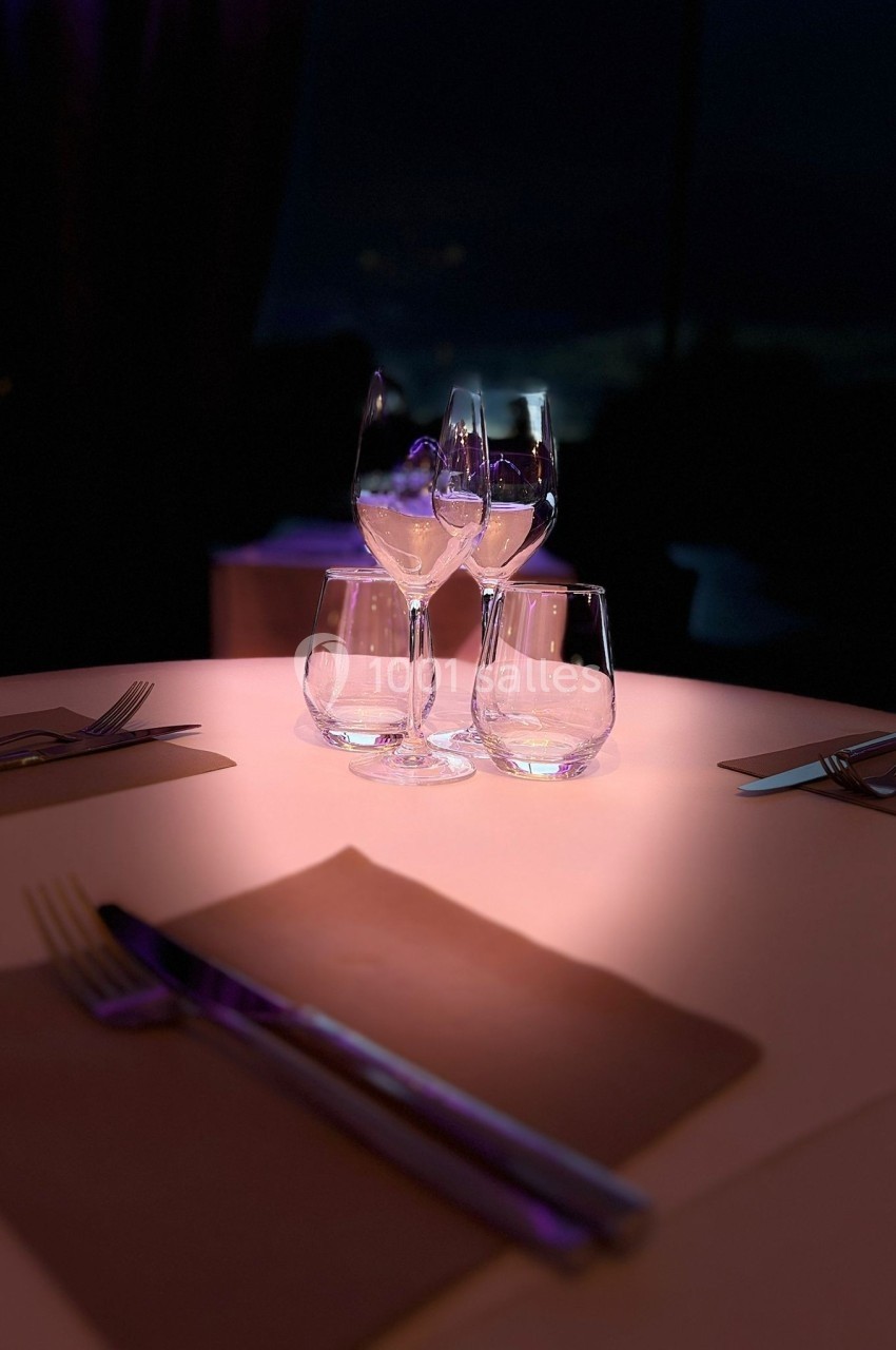 Trois verres vides posés sur une table élégamment dressée avec des couverts, éclairés par une lumière tamisée.