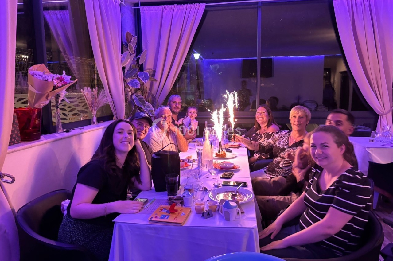 Un groupe de personnes assises autour d'une table dans un restaurant, célébrant avec des desserts et des bougies…