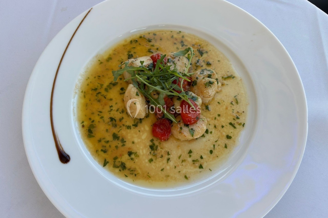Assiette de noix de Saint-Jacques dans une sauce au beurre persillé, garnie de roquette et de tomates cerises.