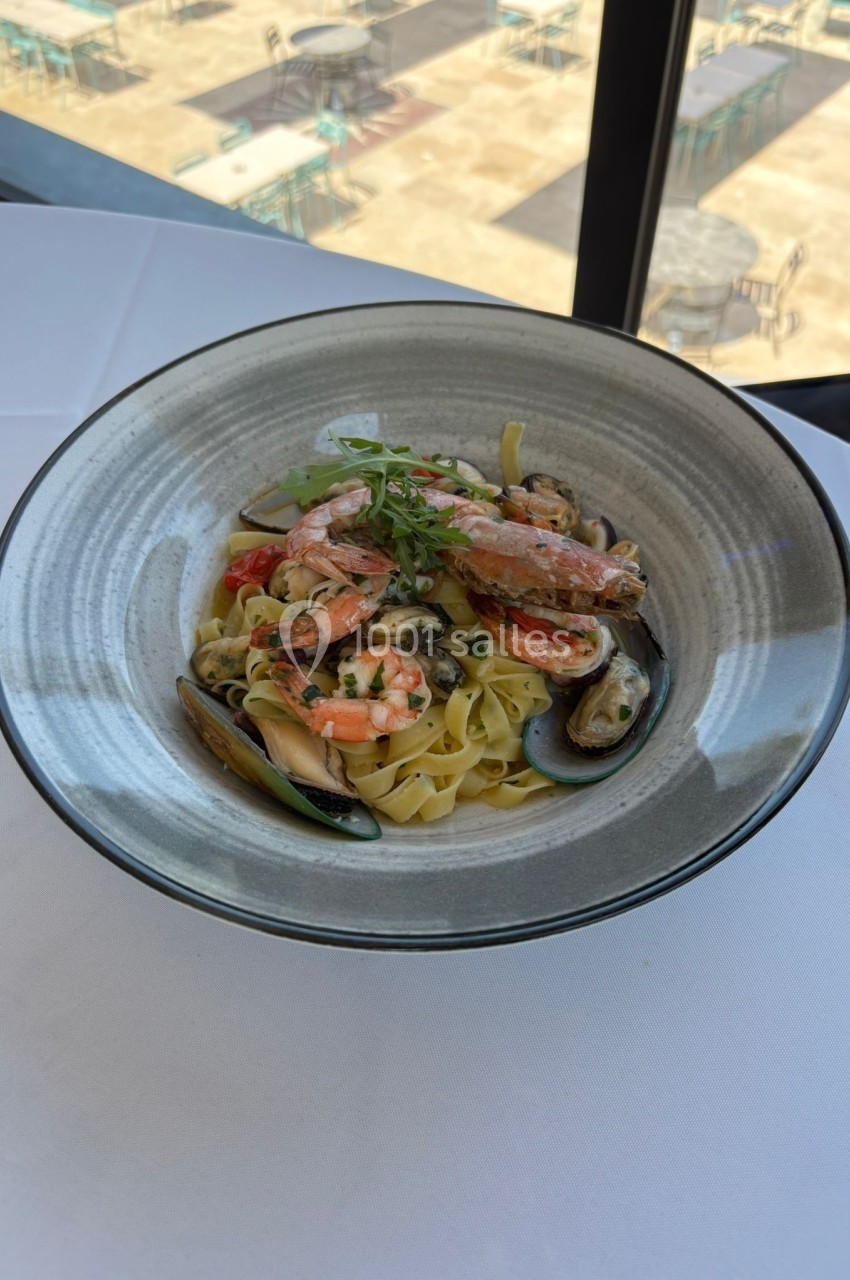 Assiette de tagliatelles aux fruits de mer avec crevettes, moules et sauce crémeuse, servie sur une nappe blanche.