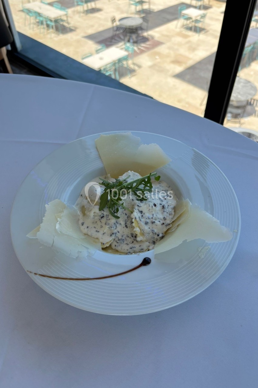 Assiette de pâtes garnies de sauce crémeuse aux truffes, copeaux de fromage et roquette, sur une nappe blanche.