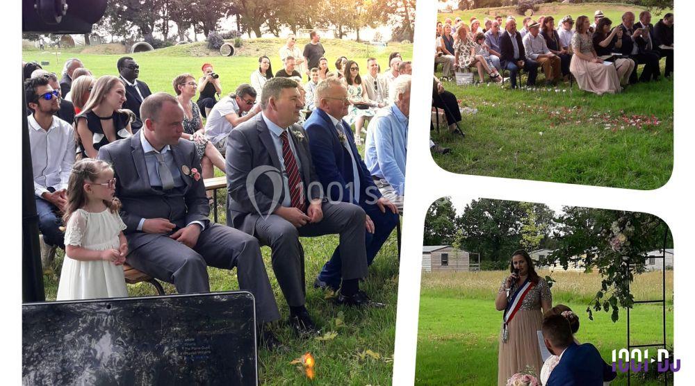 Des invités assis en plein air assistent à une cérémonie, avec une personne parlant devant un micro près d'une arche fleurie.