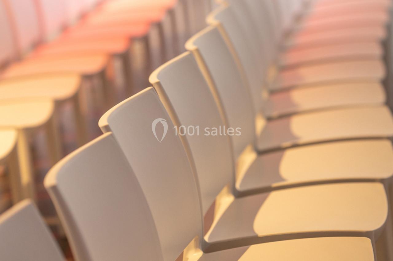 Rangée de chaises blanches alignées dans une salle éclairée par une lumière douce.