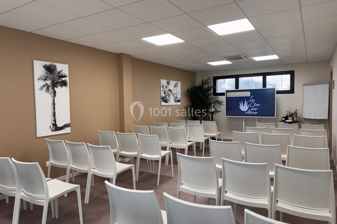 Salle de conférence lumineuse avec des chaises blanches alignées, un écran et des décorations murales.