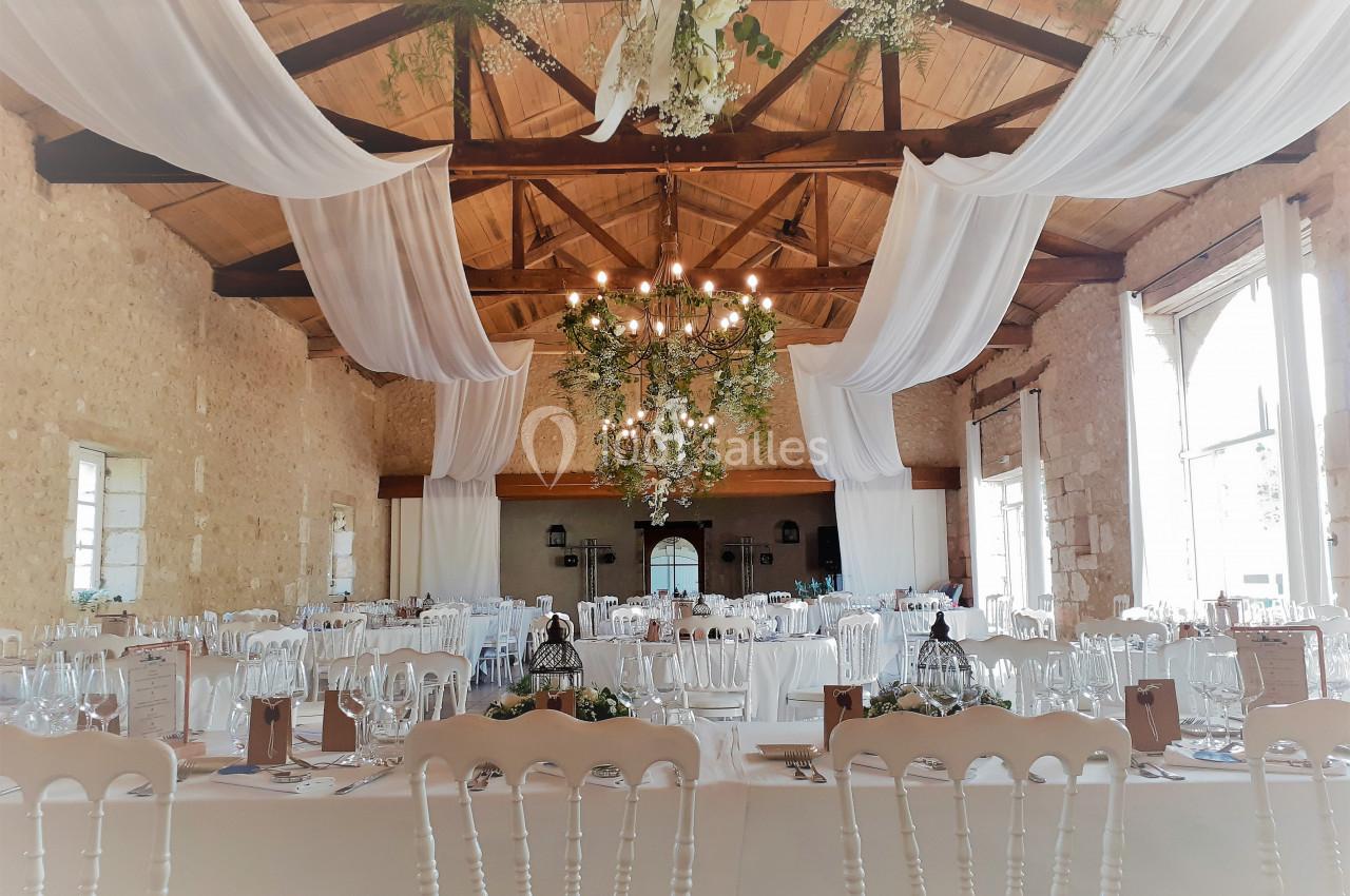 Salle de réception décorée avec des tables dressées, des nappes blanches, des chandeliers et des drapés suspendus.