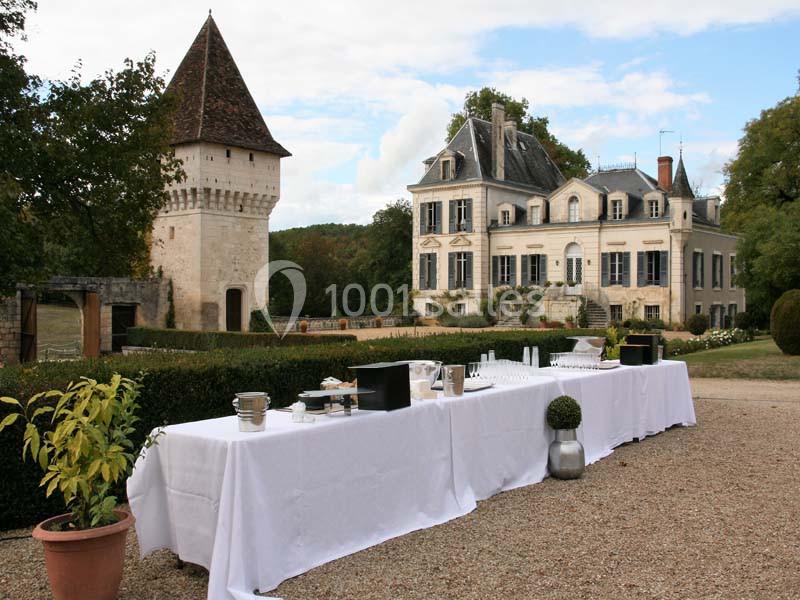 Table dressée en extérieur devant un château et une tour, entourés de verdure et d'un ciel partiellement nuageux.