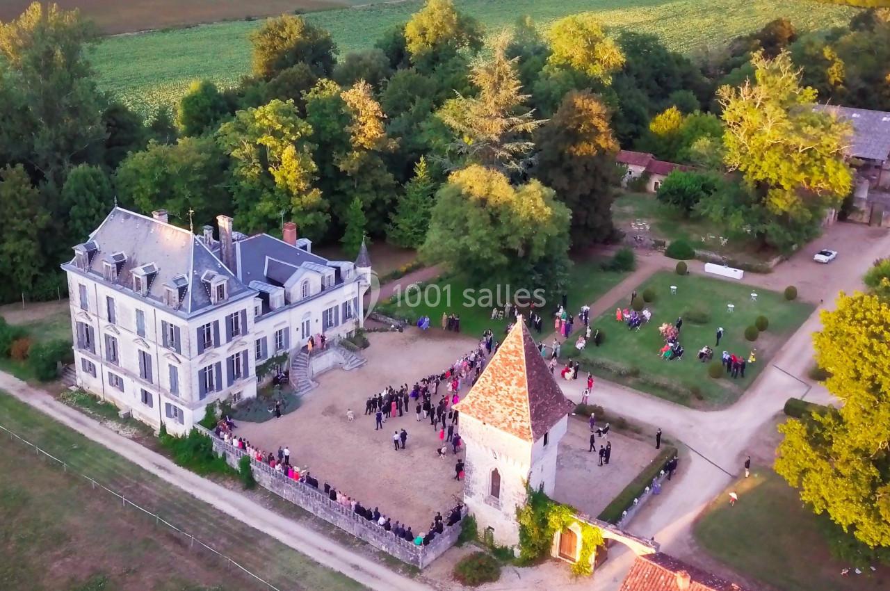 Vue aérienne d'un domaine avec une grande maison, une tour et des jardins, entouré de verdure et de visiteurs.