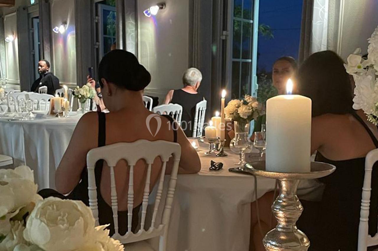 Des invités assis autour de tables décorées de bougies et de fleurs blanches dans une salle de réception en soirée.
