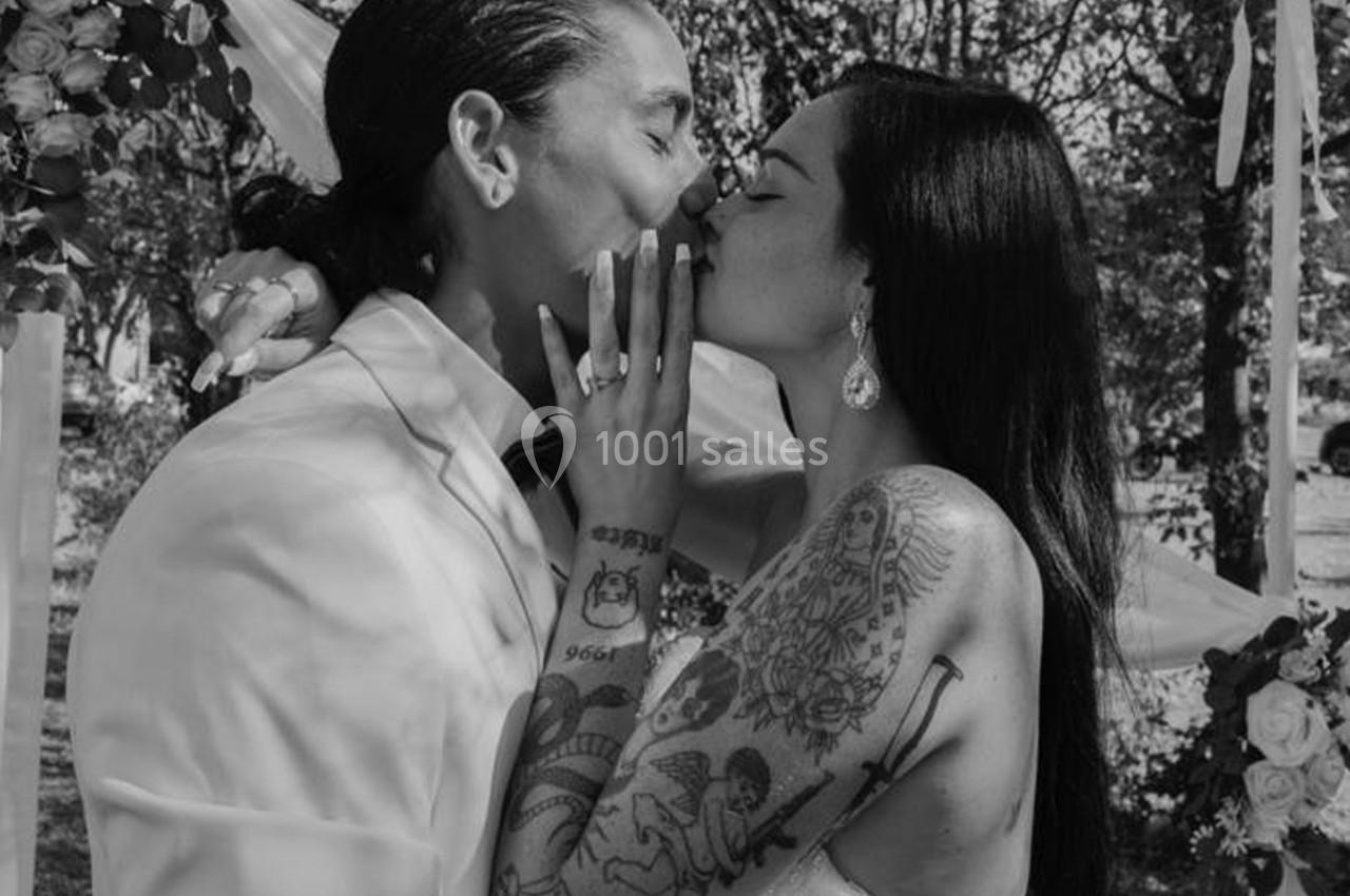 Un couple s'embrasse lors d'une cérémonie en extérieur, entouré de décorations florales.