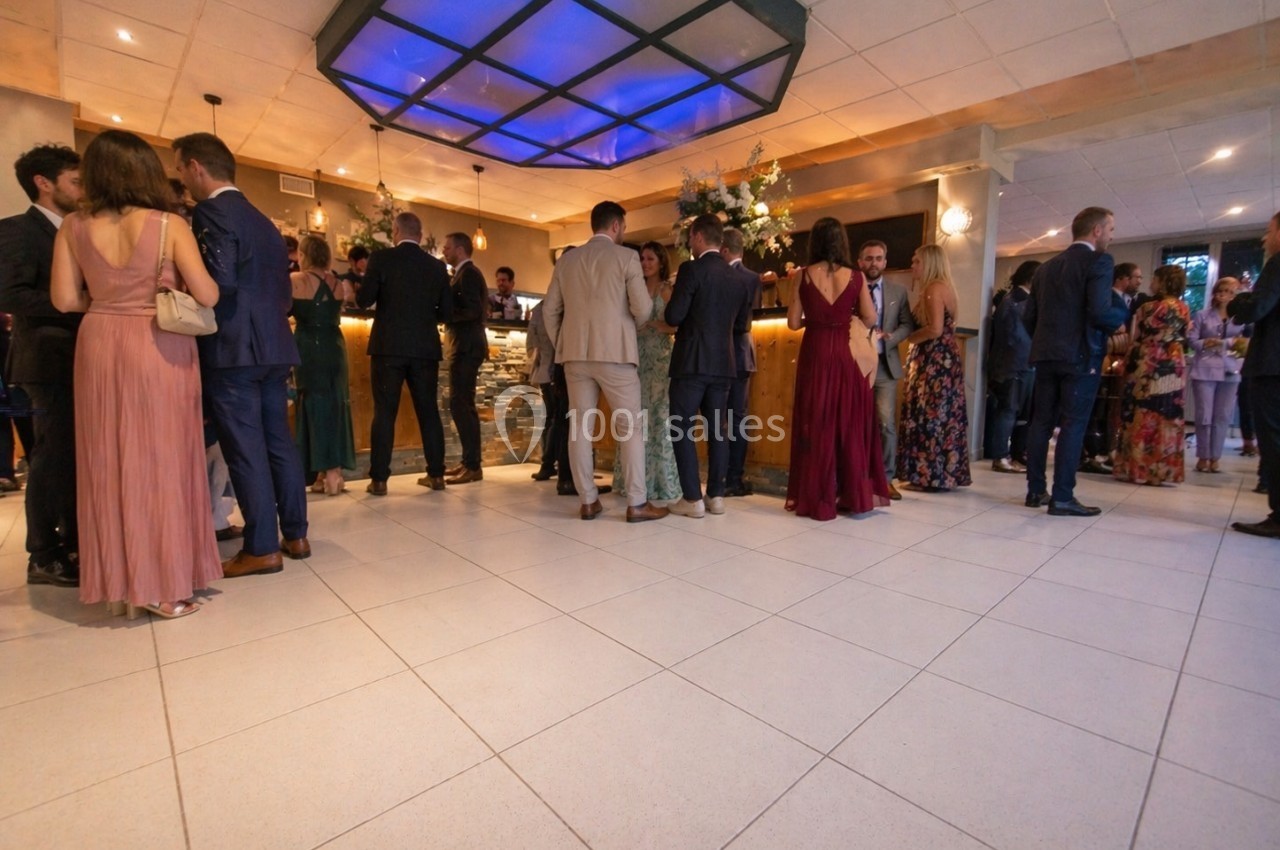 Personnes élégamment vêtues discutant debout dans un espace intérieur lumineux avec un bar en arrière-plan.