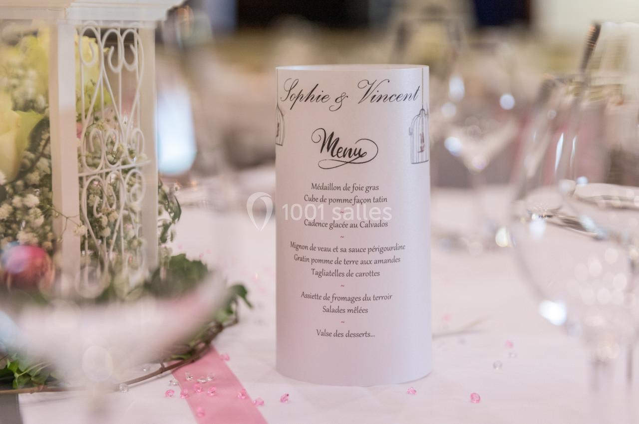Menu de mariage posé sur une table décorée avec des verres, des fleurs et des éléments de décoration élégants.