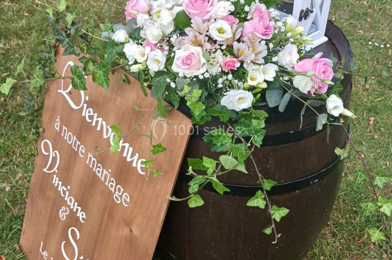 Arrangement floral avec roses et lierre sur un tonneau en bois, accompagné d'une lanterne et d'un panneau de mariage.