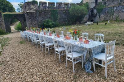 Table élégamment dressée avec nappes blanches, chaises assorties, chandeliers, fleurs roses et couverts dorés.