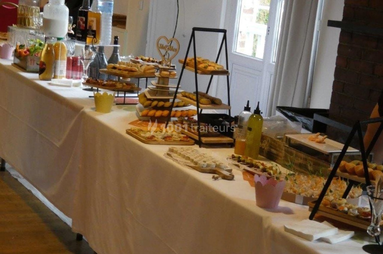 Buffet de desserts variés disposés sur une longue table blanche, avec des présentoirs et des boissons en arrière-plan.
