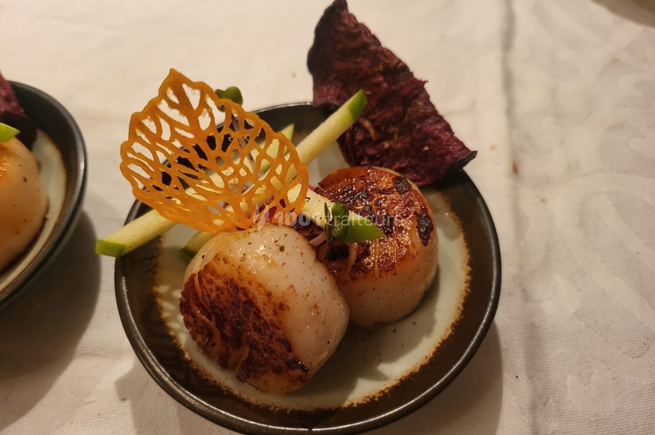 Deux noix de Saint-Jacques poêlées servies avec des décorations de chips, de pomme et une tuile croustillante.