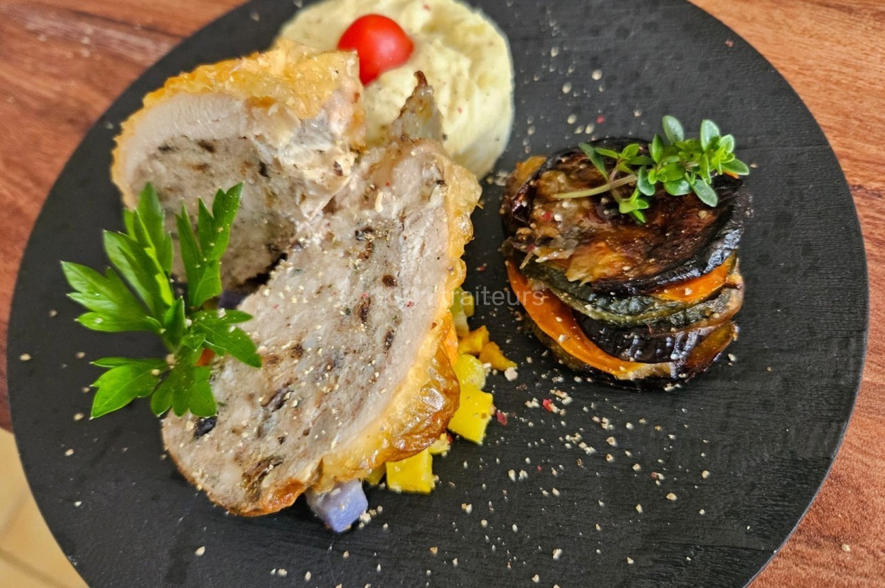 Assiette composée d'une viande farcie, d'un millefeuille de légumes grillés et d'une purée, décorée d'herbes fraîches.
