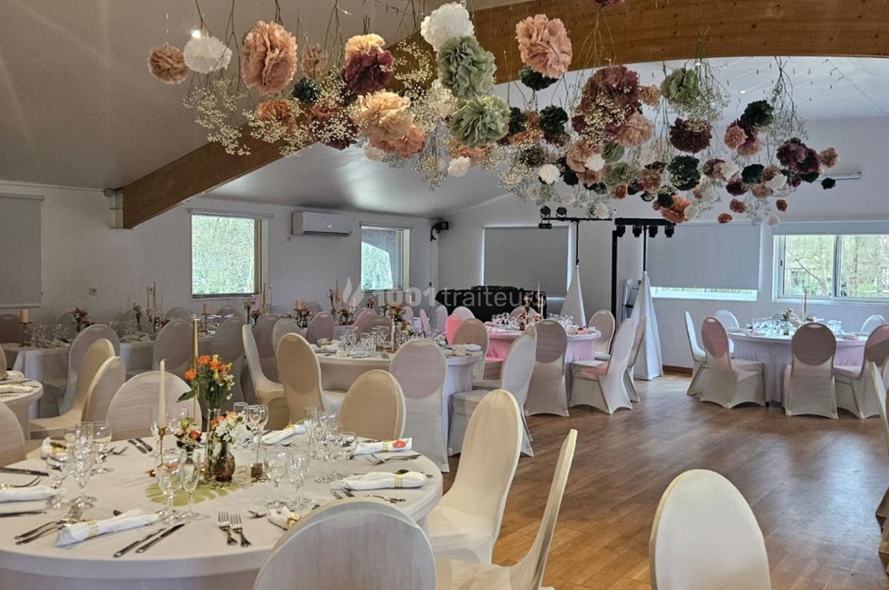 Salle de réception décorée avec des tables rondes dressées et des fleurs suspendues au plafond.