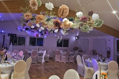 Table élégamment dressée avec nappes blanches, chaises assorties, chandeliers, fleurs roses et couverts dorés.