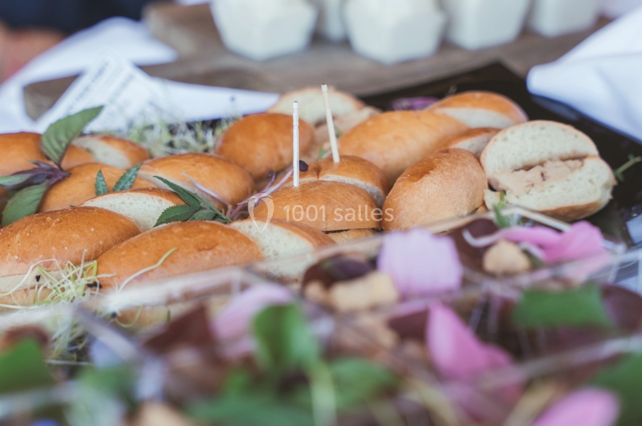 Plateau de petits sandwichs garnis, entouré de décorations végétales et d'autres amuse-bouches en arrière-plan.