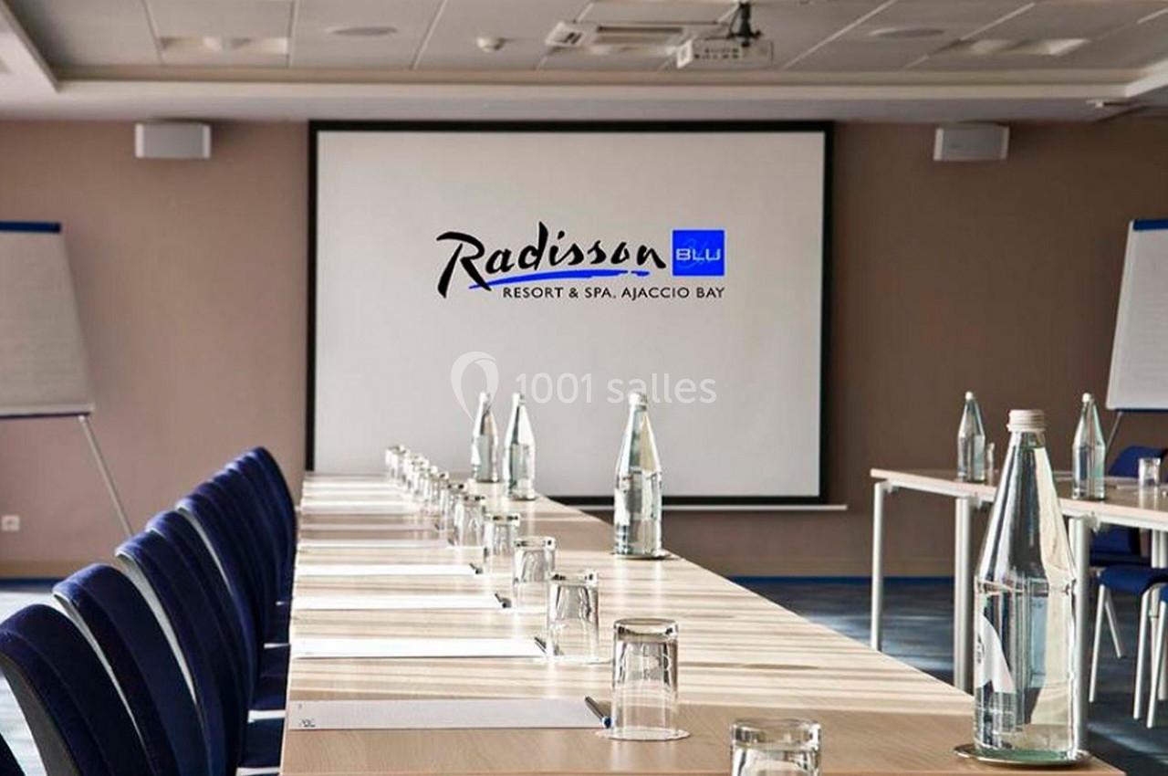 Salle de réunion avec une table longue, chaises alignées, bouteilles d'eau et un écran affichant ’Radisson Blu’.