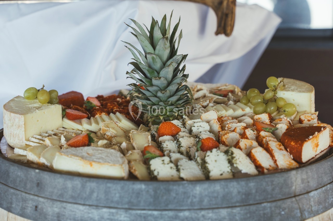 Plateau de fromages variés avec des fruits frais, dont des raisins, des fraises et un ananas au centre.