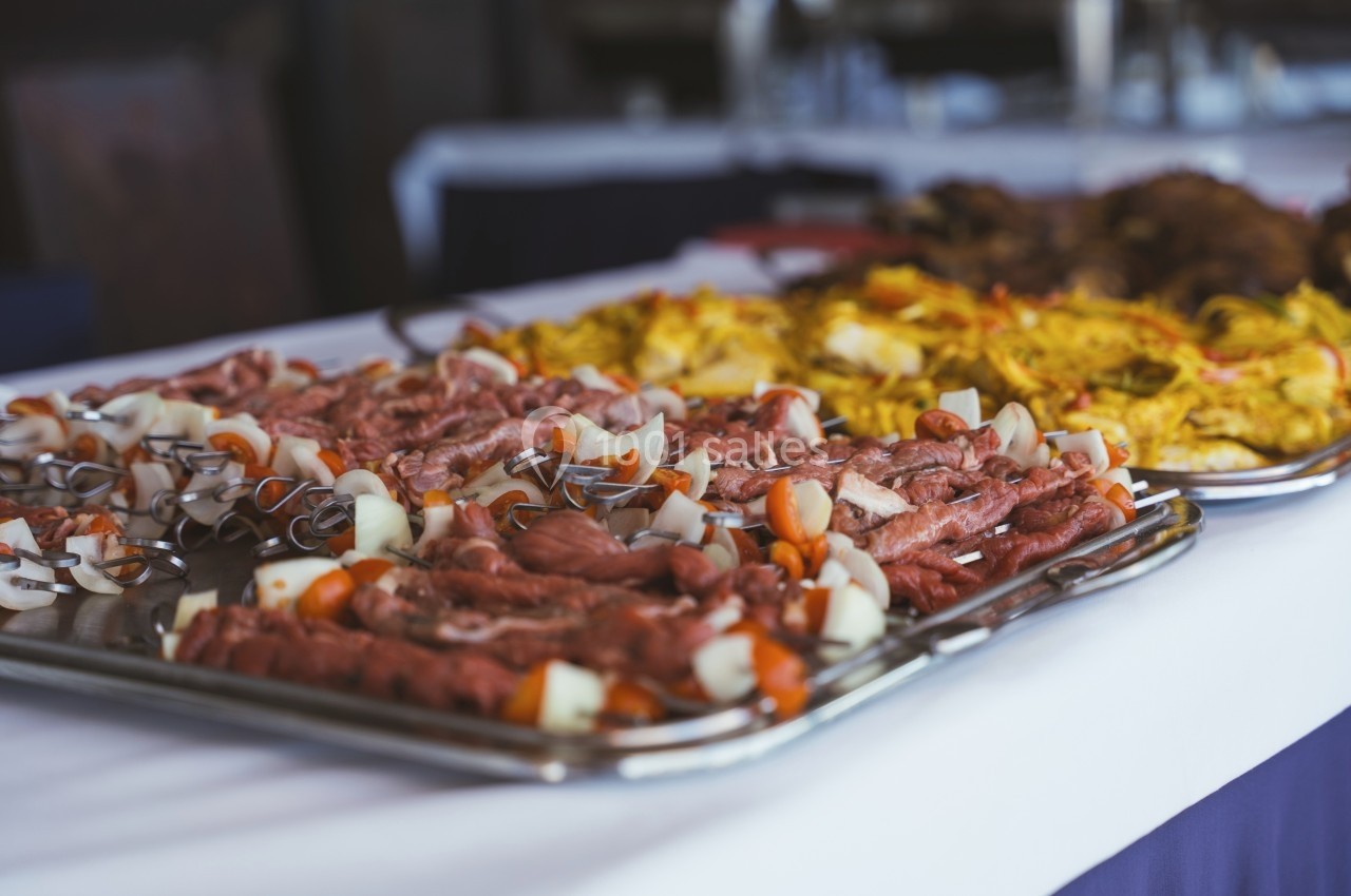 Brochettes de viande crue et légumes sur un plateau en métal, disposées sur une table avec d'autres plats.