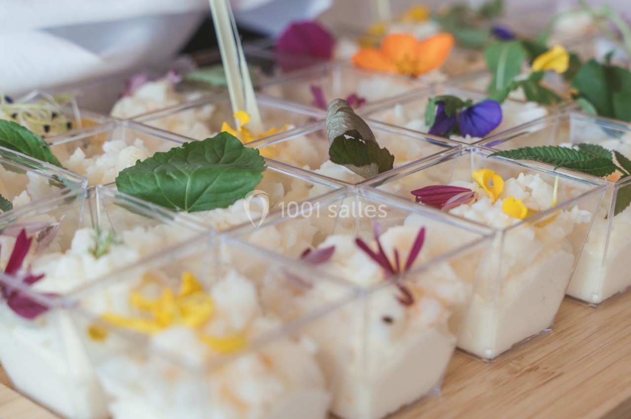 Petits verrines de mousse blanche décorées de fleurs comestibles colorées sur une table en bois.