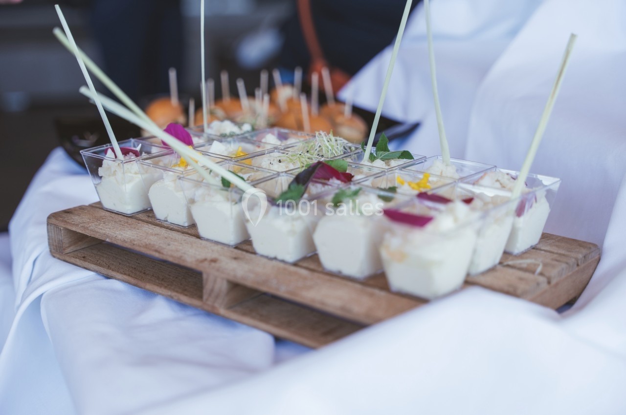 Plateau en bois avec verrines de mousse blanche garnies de fleurs et herbes, présenté sur une nappe blanche.