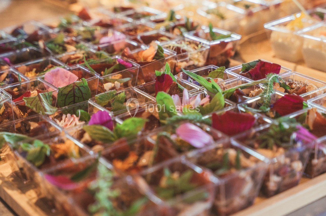 Plateaux de verrines garnies de fleurs comestibles, herbes fraîches et ingrédients variés, disposés sur une table.