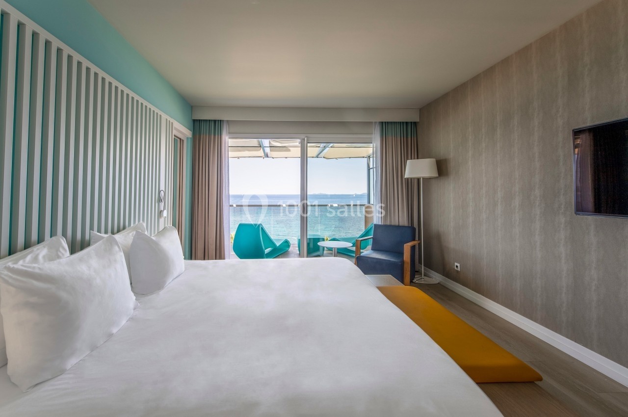Chambre lumineuse avec lit double, vue sur la mer, balcon aménagé, fauteuils colorés et décoration moderne.
