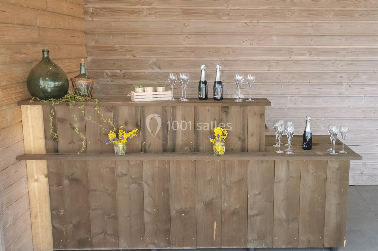 Comptoir en bois avec bouteilles de champagne, verres, fleurs jaunes et décorations dans un espace intérieur en bois.