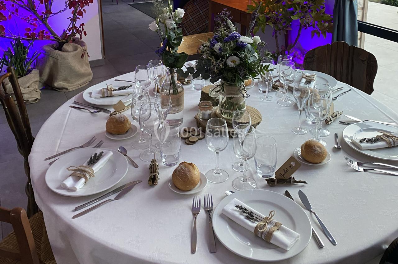 Table ronde dressée pour un repas, décorée avec des fleurs, des bougies et des serviettes ornées de brins de lavande.