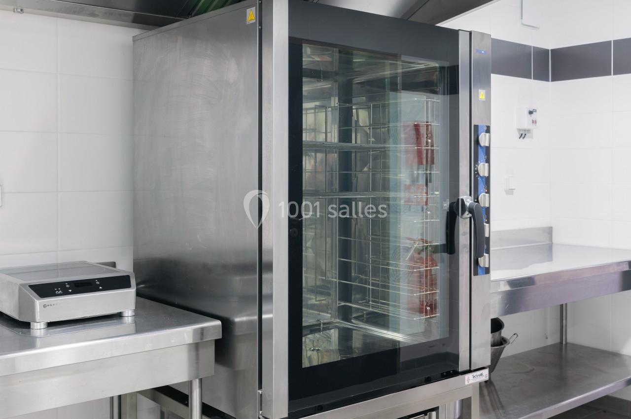 Four professionnel en acier inoxydable dans une cuisine équipée, avec balance électronique sur un plan de travail adjacent.