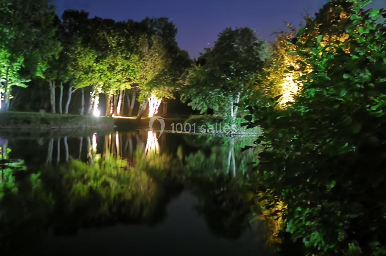 Location salle Gouville-sur-Mer (Manche) - Le Village du Phare #47 Étang entouré d'arbres illuminés la nuit, avec leurs reflets visibles sur l'eau calme.