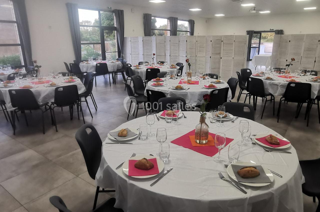 Location salle Gouville-sur-Mer (Manche) - Le Village du Phare #10 Salle de réception avec tables rondes dressées, nappes blanches, serviettes roses et vaisselle, prête pour un événement.