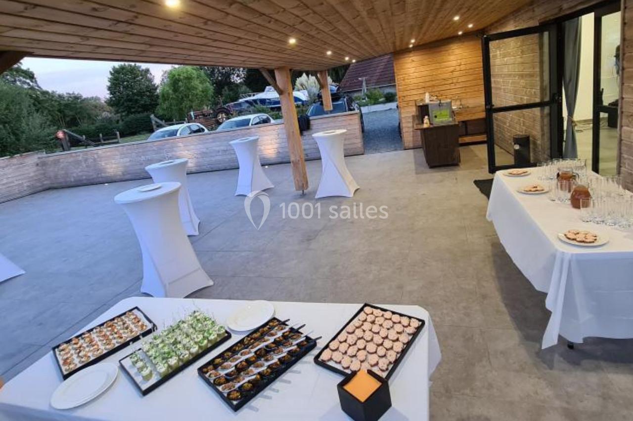 Location salle Gouville-sur-Mer (Manche) - Le Village du Phare #20 Terrasse aménagée pour un événement avec tables hautes, buffet de canapés et vue sur un espace extérieur verdoyant.