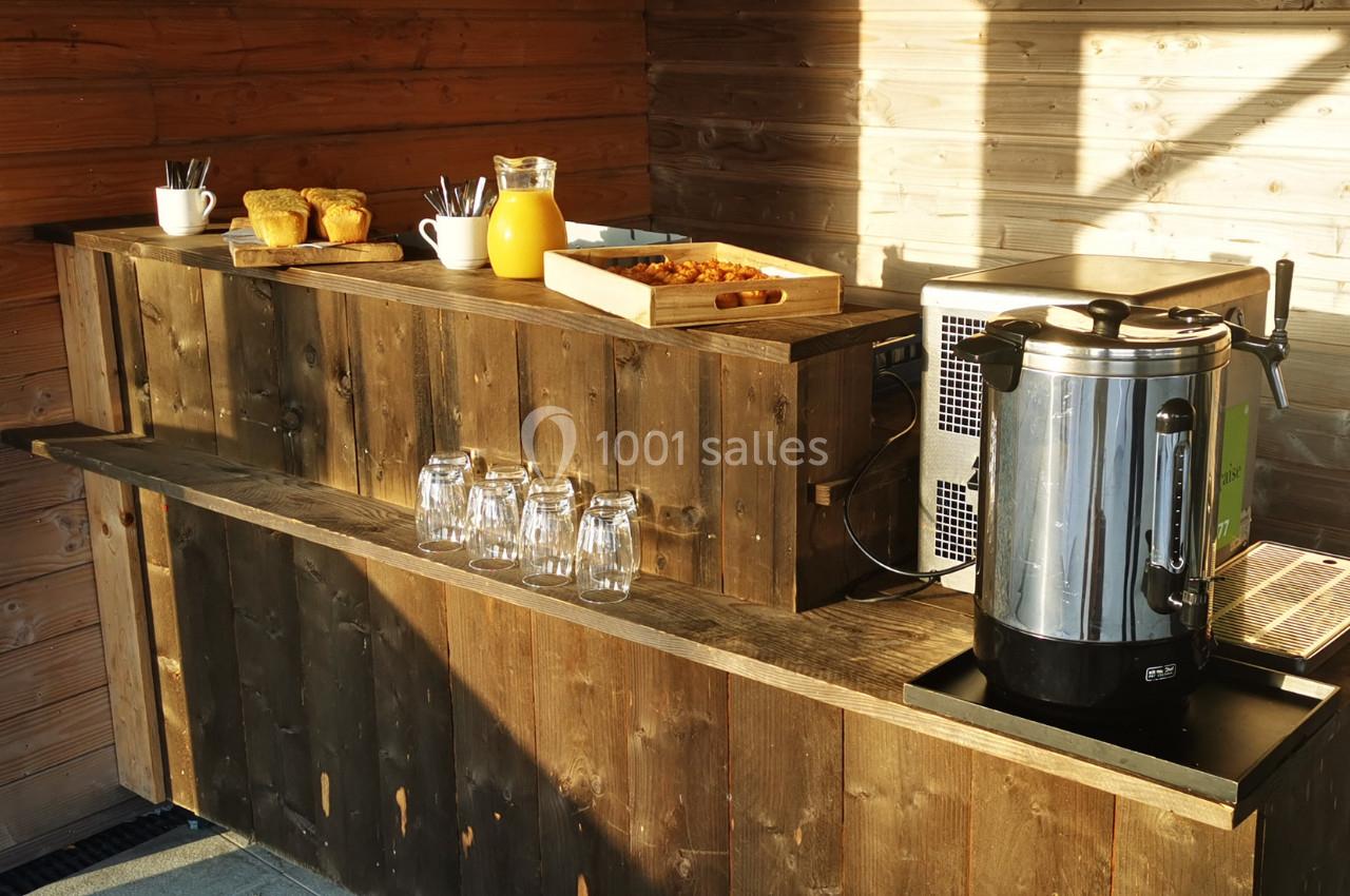 Location salle Gouville-sur-Mer (Manche) - Le Village du Phare #23 Buffet en bois avec cafetière, jus d'orange, viennoiseries, tasses et verres, éclairé par la lumière naturelle.