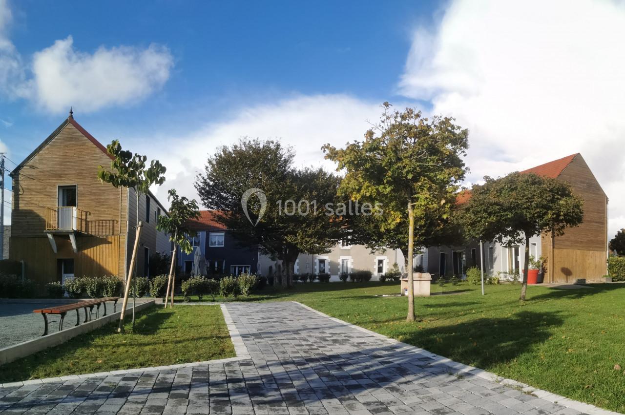 Location salle Gouville-sur-Mer (Manche) - Le Village du Phare #34 Bâtiments modernes et traditionnels entourés d'arbres, avec une allée pavée et un espace vert au premier plan.